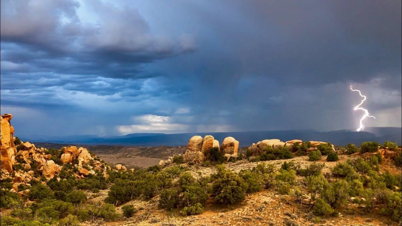 lightening touches down in the distance as rain spots the desert evening